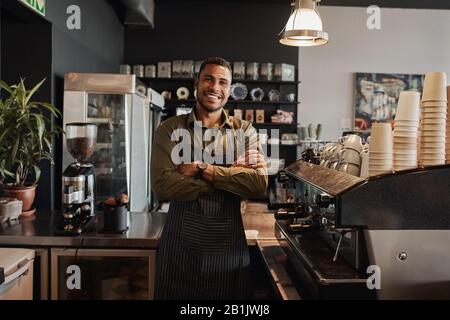 Portrait of a smiling confident young waiter standing at the cafe counter Stock Photo