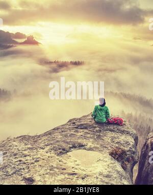 Alone travel woman hiker sits on the edge of the cliff and enjoying sunrise looking at the valley and mountains. Traveling active lifestyle concept Stock Photo