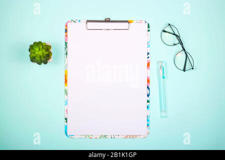 Blank paper on colored clipboard with copy space on a bright neo-mint background with glasses. Top view, flat lay. Stock Photo