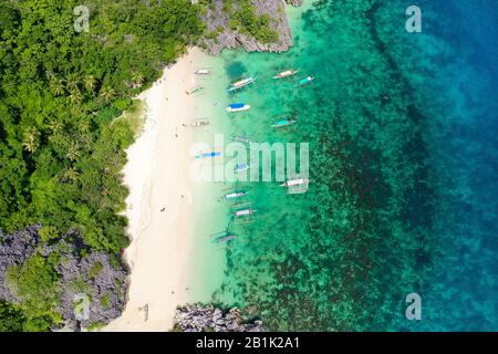 Tropical landscape: Matukad Island with beautiful beach and tourists by turquoise water view from above. Caramoan Islands, Philippines. Summer and travel vacation concept. Boats and tourists on the beach. Stock Photo