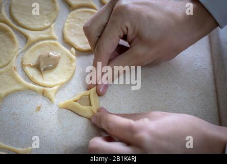 Hamantaschen. (ozenei haman) Triangular pastry made of crispy dough, stuffed with poppy, halva or chocolate. For the Jewish holiday of Purim. Hands in Stock Photo