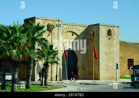 Meknes, Morocco - November 18th 2014: Unidentified people in front of the city wall with gate and place with palm trees Stock Photo