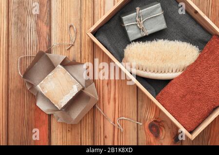 Handmade soap wrapped in craft paper, towel and massage brush lie in a wooden box on a wooden background. Stock Photo