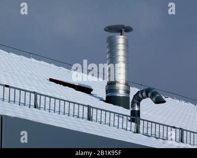 aluminum roof vents under blue sky on snowy sloped roof. galvanized steel snow and ice guard grille.  winter day in bright light. building ventilation Stock Photo