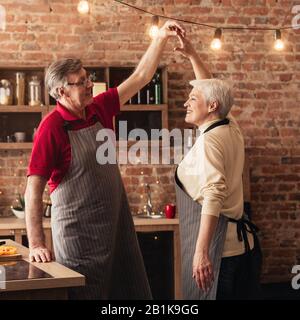 Affectionate seniour couple cooking and dancing together in kitchen Stock Photo