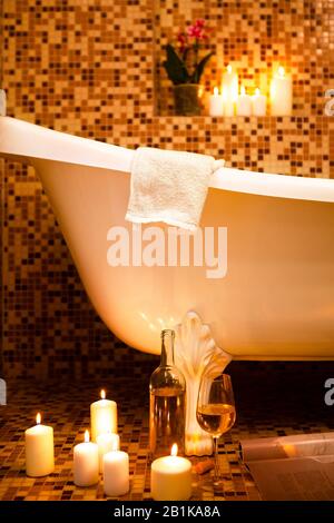 Luxury vintage bathtub in bathroom with orange mosaic ceramic tile floor and walls decorated with burning candles Stock Photo
