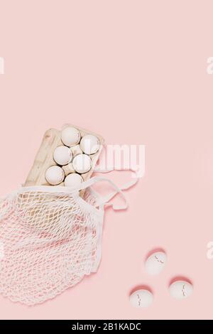 Happy Easter. White eggs with painted eyes in paper packaging and white mesh bag on pink background. Flat lay, top view, copy space. Stock Photo