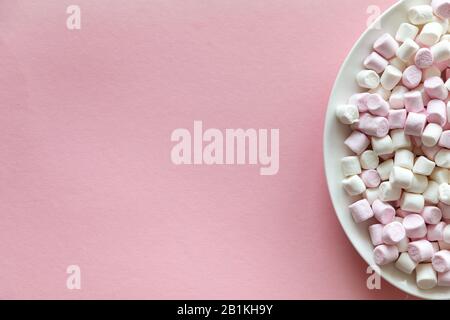 Pink and white mini marshmallows in white plate on pink background with free space for text Stock Photo