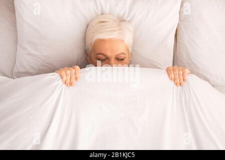 Retired lady lying in bed and playing hide-and-seek Stock Photo