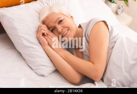 Calm senior woman lying in bed and smiling Stock Photo
