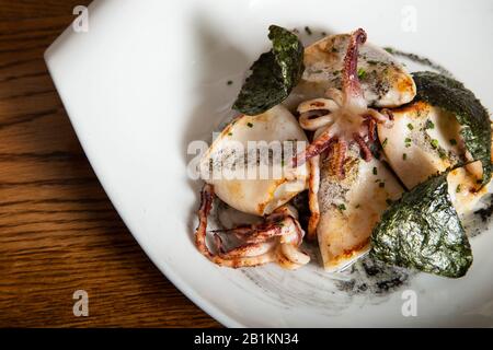 Grilled squid with sauteed black sausage, candied onion and crispy nori seaweed served in white porcelain dish. Novel cuisine. isolated image Stock Photo
