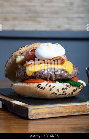 Delicious homemade beef burger, poached egg, hollandaise sauce and crispy bacon on wooden board. Vertical image Stock Photo