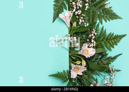 Creative layout made of fern green leaves and white flowers with paper card note. Flat lay. Spring concept