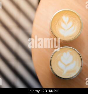 Coffee with a pattern on a foam in two glasses. Against the background of the table and striped tiles in blur. Photo taken from above. Stock Photo