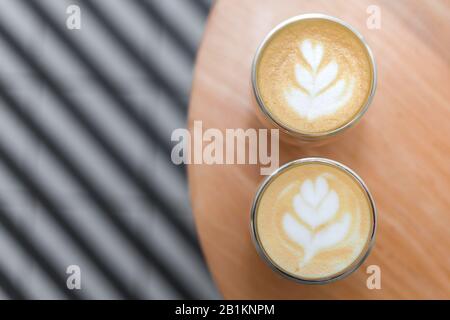 Coffee with a pattern on a foam in two glasses. Against the background of the table and striped tiles in blur. Photo taken from above. Stock Photo