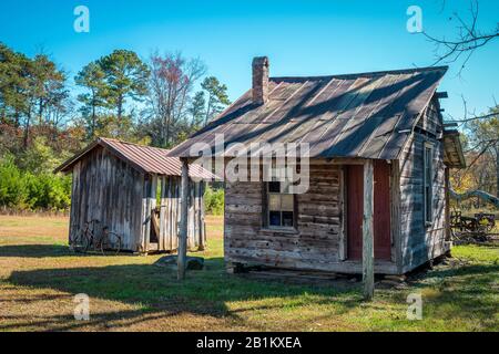 A small abandoned homestead with a shed and bicycle next to it in the north Georgia mountains still standing weathered and decaying on a sunny day in Stock Photo