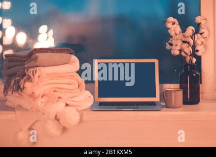 Stack of knitted plaids with gray mug and computer on cozy window Stock Photo
