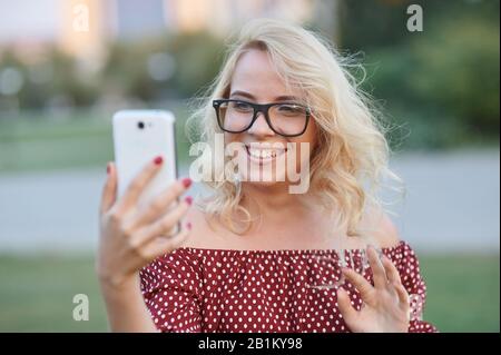 beautiful young woman blogger with blonde hair take photo on smartphone at the city street background. pretty girl having smart phone Stock Photo