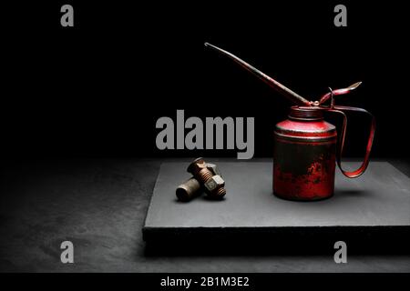 Red oilcan with rusted dirty old bolts and nuts on a black dark background fine art in studio Stock Photo