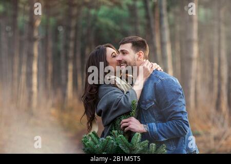 Happy man and woman in warm clothes carrying Christmas fir tree together walking on path in woods Stock Photo
