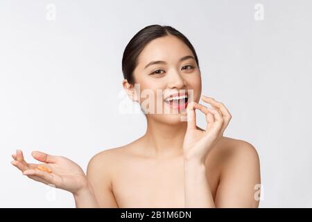 Young attractive asian woman who takes a capsule or pill. Isolated over white background. Stock Photo