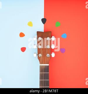 Colorful picks around acoustic guitars headstock. Flat lay on light blue and red background Stock Photo