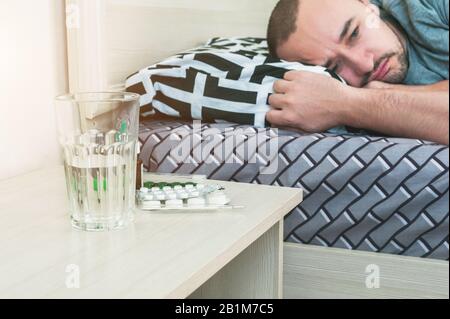 A sick person is lying in bed, pills and medicines on the table. Stock Photo