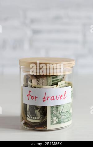 Money savings for travel in a glass jar on white wood table over white brick wall. Savings for travel budget concept. Stock Photo