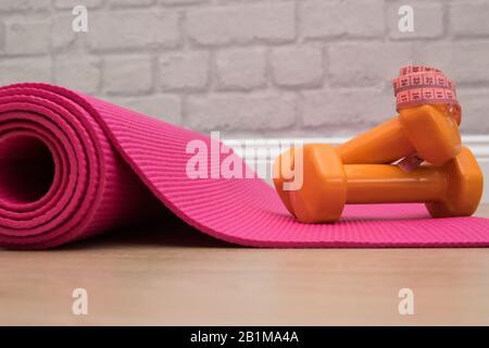Two orange dumbbells on a pink yoga mat in fitness studie. A tools for training, sport and activity in summer time. Stock Photo