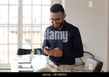 Millennial middle eastern ethnicity businessman using smartphone apps in office Stock Photo