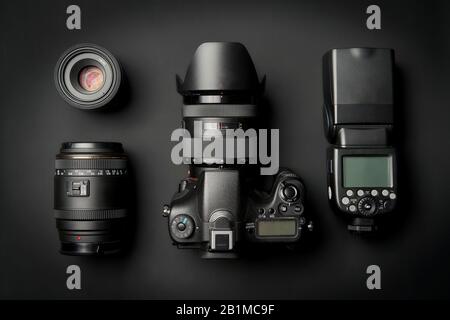 top view of modern digital camera equipment - DSLR with attached zoom lens and hood, lenses and external flashlight on black surface Stock Photo