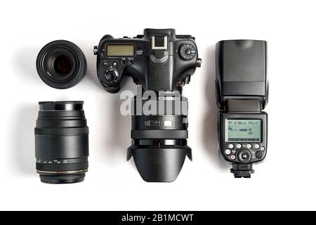 top view of modern digital camera equipment - DSLR with attached zoom lens and hood, lenses and external flashlight on white background Stock Photo