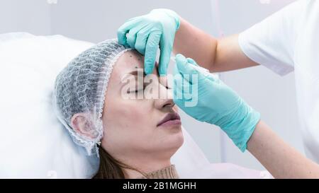 The young beautician doctor preparing to making injection in female forehead. The doctor cosmetologist makes anti-aging treatment and face lift proced Stock Photo