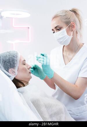 The young beautician doctor preparing to making injection in female forehead. The doctor cosmetologist makes anti-aging treatment and face lift proced Stock Photo