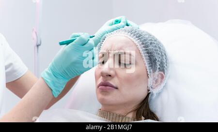 The young beautician doctor preparing to making injection in female forehead. The doctor cosmetologist makes anti-aging treatment and face lift proced Stock Photo