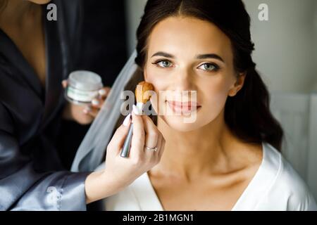 Young woman stylist doing makeup beautiful bride in beauty salon Stock Photo