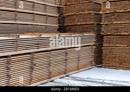 Large stacks of wooden planks background with selective focus and linear perspective. Winter woodwork industrial storage. Stock Photo