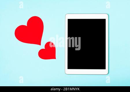 Tablet on a blue background with cute hearts. The concept of meeting website, love in internet, love to your gadget and technology, love correspondence, Valentine's Day, surprise. Flat lay Stock Photo