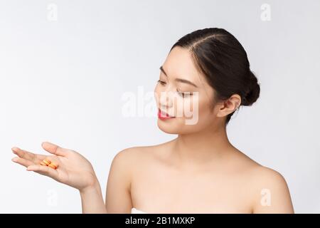 Young attractive asian woman who takes a capsule or pill. Isolated over white background. Stock Photo