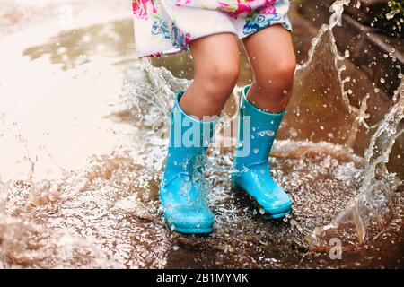 Playful excited preschool child in casual clothes and rubber boots with blue umbrella laughing and jumping in puddle smiling at camera while playing i Stock Photo Alamy