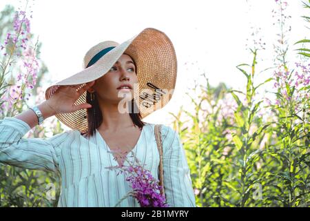 Beautiful woman in a big hat enjoing the sun on a field with flowers. Summer lifestyle. Outdoor Stock Photo