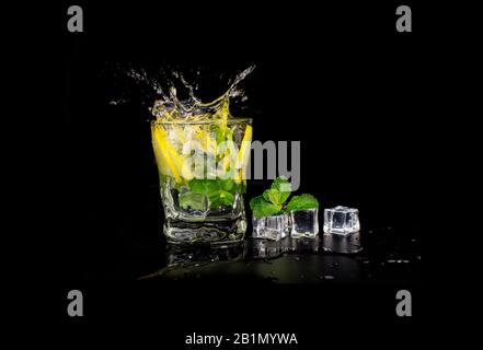 mojito cocktail drink with mint and lemon lime in a glass splash splashing out of a glass with ice cubes, drops and splashes on a black background Stock Photo