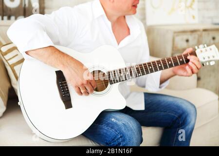 Unrecognizable male playing acoustic guitar while sitting in armchair and resting at home Stock Photo
