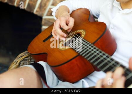 Unrecognizable male playing acoustic guitar while sitting in armchair and resting at home Stock Photo