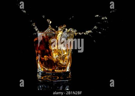 splash alcohol drink whiskey with ice with drops in a glass on a black background Stock Photo