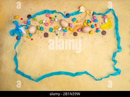 Colorful Easter eggs, sweets on yellow background, with blue ribbon and festive bow decoration, copy space Stock Photo