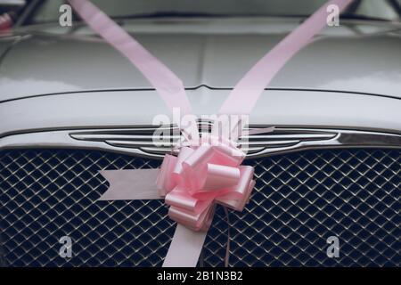 a pink wedding ribbon with a bow tied around a silver car ready to be used as a wedding car Stock Photo