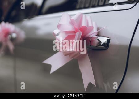 a pink bow made of ribbon on the door handle of a wedding car or wedding limousine Stock Photo
