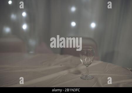a single empty glass on a table covered in a white table cloth at a party or reception Stock Photo