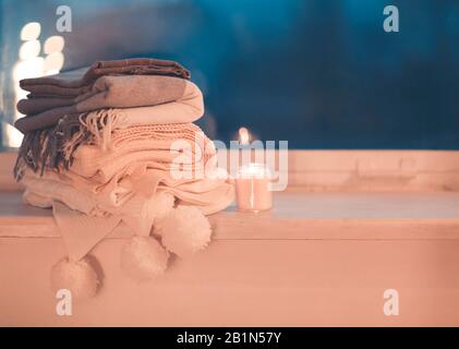 Stack of knitted plaids with gray mug and burning candle on cozy window Stock Photo